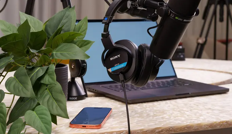 A well-equipped podcast studio featuring a laptop, microphone, headphones, and a smartphone on a stylish desk
