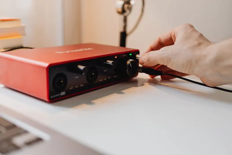 A close-up of a hand adjusting controls on a red audio interface, emphasizing technology use