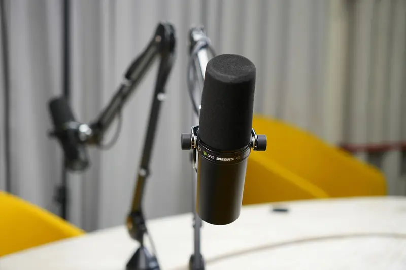 Close-up of a dynamic microphone in a modern podcast studio setup with boom arms