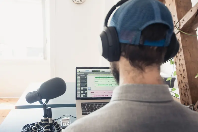 Podcaster wearing headphones works on audio editing with laptop and microphone in a home setup