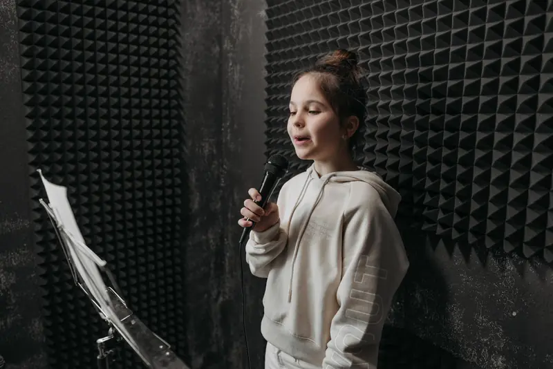 A young girl sings into a microphone in a soundproof room with acoustic panels around her