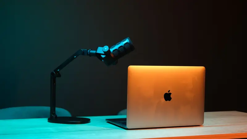 Illuminated modern podcast setup with a microphone and laptop on a wooden desk