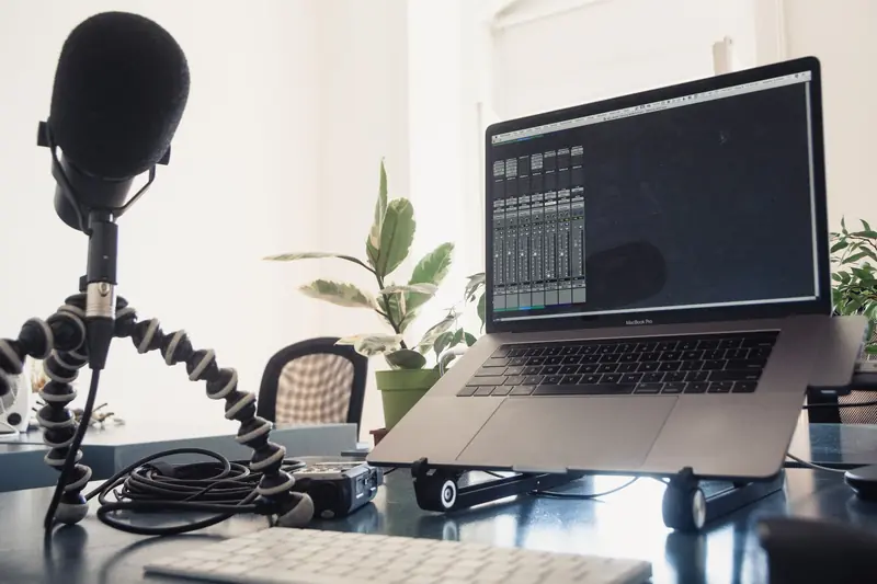 A detailed studio setup featuring a laptop and microphone on a desk for audio production