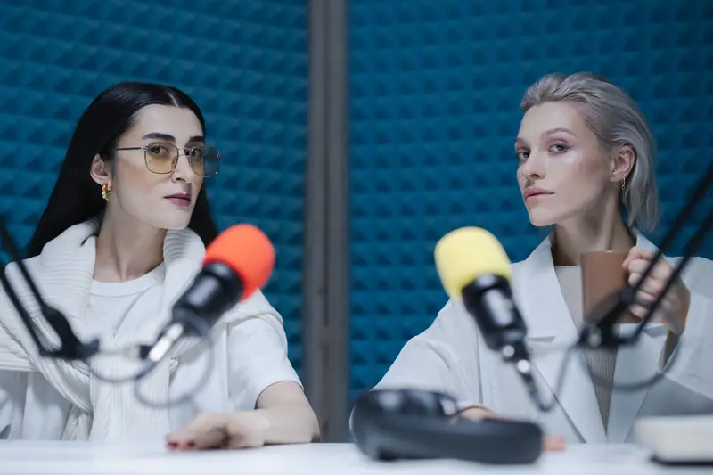 Two women in a soundproof studio with microphones, recording a podcast